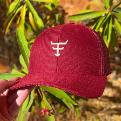 Boné vinho Texas Farm com tela, bordado branco na frente, segurado por uma mão em ambiente ao ar livre