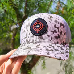 Boné Goyazes com padrão pixels verdes e tela cinza, exibindo um patch preto com alvo vermelho.