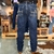 Calça masculina azul escura com detalhes nos bolsos traseiros, vista de trás, em ambiente de loja.