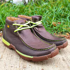 Tênis Destroyer Goyazes na cor tabaco verde, com detalhes em neon, sobre uma superfície de concreto e grama ao fundo.