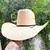 Chapéu Palha Lone Star Bulls Mex Branco com aba larga, segurado por uma mão, em fundo com folhas verdes.