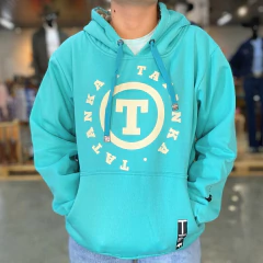 Moletom unissex azul claro com capuz e logo branco da marca Tatanka na frente, modelo vestindo com as mãos no bolso