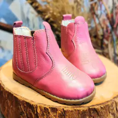 Botina infantil rosa pink com detalhes em costura, sobre uma superfície de madeira.