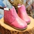 Botina infantil rosa pink com detalhes em costura, sobre uma superfície de madeira.