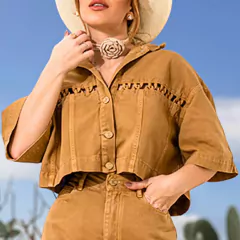 Mulher usando uma camisa cropped caqui com botões e detalhes de costura, em um cenário ao ar livre.