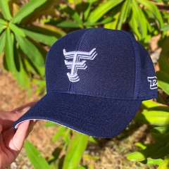 Boné azul marinho Texas Farm com logo branco bordado na frente, segurado por uma mão em fundo de plantas verdes