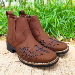 Botina feminina D'Milton Floter preta com detalhes em relevo, sobre fundo de grama e piso de concreto.