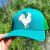 Boné trucker na cor turquesa com estampa de um galo em relevo.