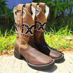 Bota Texas Star Fossil Café com detalhe em couro e emblema, posicionada sobre a grama e calçada.