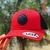 Boné Tuff vermelho com detalhe em preto e logo emborrachado, segurado por uma mão ao ar livre.