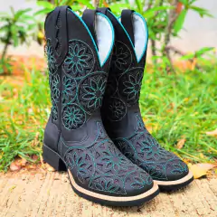 Bota feminina da marca Fort Boots com brilho preto e verde, detalhadamente bordada com flores, em um fundo de grama.