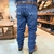 Calça masculina azul Bill Way com detalhes bordados, vista traseira, em ambiente de loja.