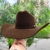 Chapéu Eldorado Cattleman marrom com forro, sendo segurado por uma mão, em um fundo verde.