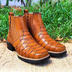 Botina Zero Impacto Escamada Whisk Bico Quadrado em tom marrom, destacando seu design escamado e bico quadrado, posicionada sobre uma superfície de concreto com grama ao fundo.