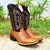 Bota masculina texana Mr. West com bordado laranja, em fundo verde de grama.