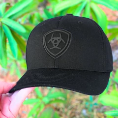 Boné preto Flexfit da marca Ariat, com logotipo em relevo na parte frontal, segurado por uma mão.