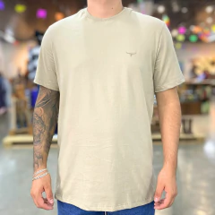 Camiseta masculina bege ecru tradicional com bordado discreto no peito, usada por homem com tatuagem no braço esquerdo