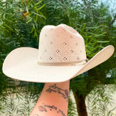 Chapéu Eldorado 15x Bristol branco sendo segurado por um braço com tatuagens, ao fundo folhagens verdes desfocadas