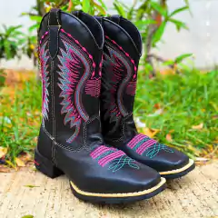 Bota feminina Tex Team preta com detalhes em bordado colorido, posicionada em um terreno natural.