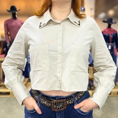 Camisa cropped feminina bege com botões frontais, bolsos no peito e detalhes metálicos na gola, usada com cinto e calça jeans