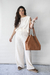 Modelo usando una blusa blanca de lino con pantalones amplios, sosteniendo un bolso de cuero marrón.