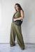 Mujer posando con blusa verde oliva y pantalones anchos, sosteniendo un bolso negro.