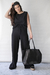 Modelo luciendo una blusa negra de la colección Milos By SAHA, con pantalones y un bolso negro en un fondo claro.