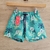 Short de baño para niños con estampado tropical en tonos verdes y flores blancas.