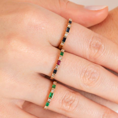 Anéis em ouro 14K com esmeraldas, diamantes e pedras coloridas, exibidos em mãos.