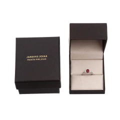 Anel de ouro com pedra de rubi oval e diamantes laterais em caixa preta de joias Jardins Joias.