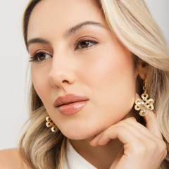 Mulher loira usando brinco dourado H. Stern com design de nó búdico