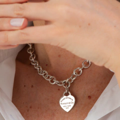 Colar de elos Tiffany com berloque em forma de coração, utilizado por uma pessoa.