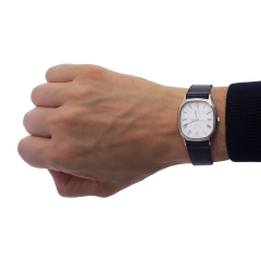 Relógio Omega De Ville em um pulso masculino, mostrando o mostrador prateado e a pulseira de couro preta.