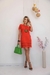 Modelo usando um vestido curto vermelho com mangas curtas e gola redonda, detalhes em linhas pretas, segurando uma bolsa verde.