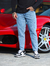 Homem usando calça slim fit jeans casual claro ao lado de um carro esportivo vermelho.