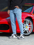 Homem usando calça slim fit jeans casual claro ao lado de um carro esportivo vermelho.