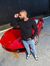 Homem usando calça slim fit jeans casual claro, óculos de sol e camiseta preta, posando ao lado de um carro esportivo vermelho.