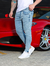 Homem usando calça skinny jeans clara ao lado de um carro esportivo vermelho.