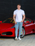 Homem posando ao lado de um carro esportivo vermelho, usando calça skinny jeans clara e camiseta branca.