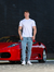 Modelo usando calça skinny jeans clara, camiseta branca, ao lado de um carro esportivo vermelho.