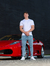Modelo masculino vestindo calça skinny jeans clara ao lado de um carro esportivo vermelho.