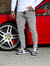Homem usando calça skinny jeans casual marmorizada cinza, com tênis preto e branco, ao lado de um carro vermelho.