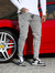 Homem usando calça skinny jeans casual marmorizada cinza ao lado de um carro esportivo vermelho.