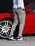 Homem usando calça skinny jeans casual marmorizada cinza ao lado de um carro esportivo vermelho.