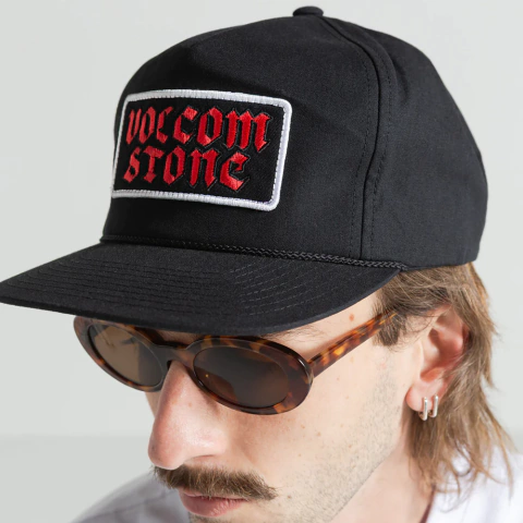 Boné Volcom No Brainer preto com patch bordado "Volcom Stone" em vermelho, modelo usando óculos de sol e brincos.