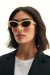Mulher usando óculos de sol feminino modelo Dora Vanilla com armação em tom claro e lentes escuras.