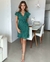 Modelo vestindo um vestido envelope verde com poás brancos, destacando-se em um ambiente moderno e iluminado.