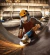Trabajador con casco y protección usando amoladora angular Bosch para cortar metal generando chispas en un taller industrial