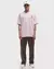 Homem usando camiseta rosa da Nike com estampa de coração para o Dia dos Namorados, combinada com calças marrons e boné branco.