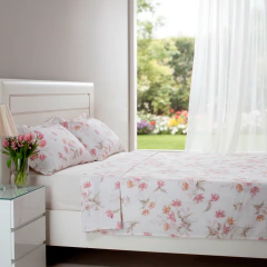 Jogo de lençol king size com estampa floral em algodão percal 200 fios, 4 peças, em cama branca ao lado de mesa de cabeceira com vaso de flores